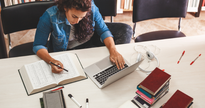 female-student-at-desk-in-library-studying-with-books-and-laptop