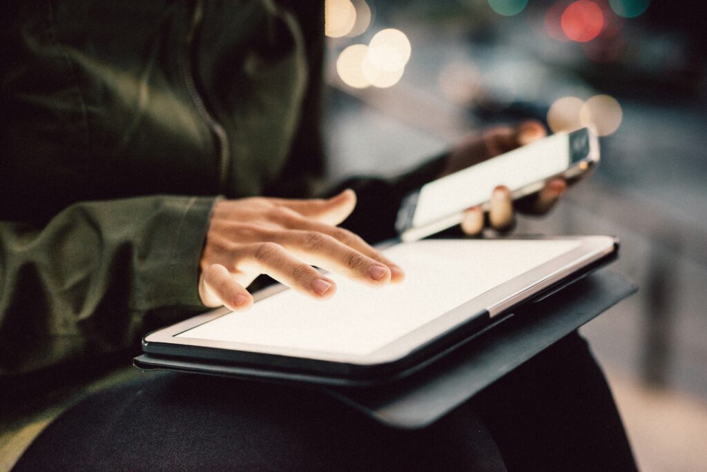 Close up on the hands of young woman using smartphone and tablet in the city night, pointing and touching the screen with her finger - technology, multitasking, communication concept