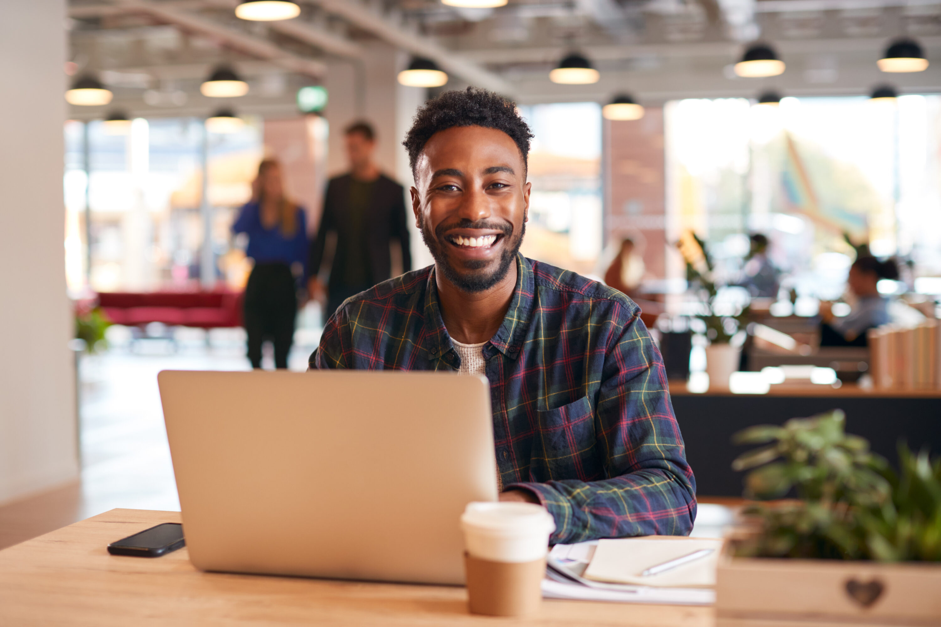 Portrait Of Smiling Businessman Sitting At Desk With Laptop In Modern Open Plan Office