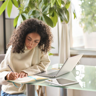 Young woman, girl student using laptop elearning or remote working at home office using laptop pc computer for webinar, learning online training digital education sitting at table, writing notes.