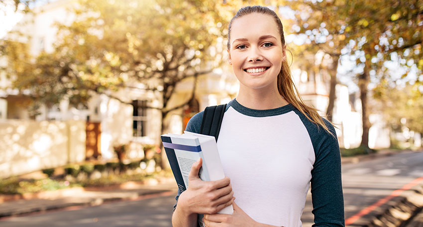 A female law student stands confidently at her law school campus with textbooks in her hands